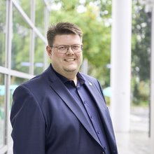 Foto von Jörg Fritzsche im blauen Jacket mit Anstecknadel mit dem Sonnenblumenlogo der Grünen vor dem Hagener Rathaus