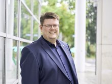 Foto von Jörg Fritzsche im blauen Jacket mit Anstecknadel mit dem Sonnenblumenlogo der Grünen vor dem Hagener Rathaus