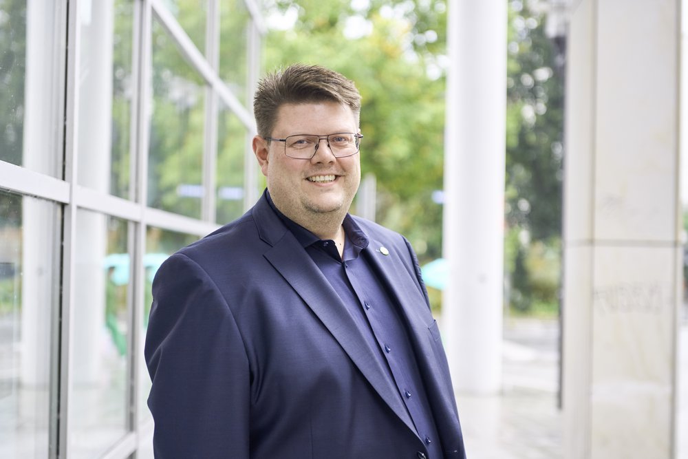 Foto von Jörg Fritzsche im blauen Jacket mit Anstecknadel mit dem Sonnenblumenlogo der Grünen vor dem Hagener Rathaus